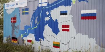 Nápis "Nord Stream 2 Committed. Spoľahlivý. Bezpečný." visí nad namaľovanou mapou plynovodu Nord Stream 2 z Ruska do Nemecka na odbernej stanici zemného plynu v priemyselnej zóne Lubmin v nemeckom Lubmine 16. novembra 2021 (Foto: SITA/AP/Stefan Sauer/dpa)