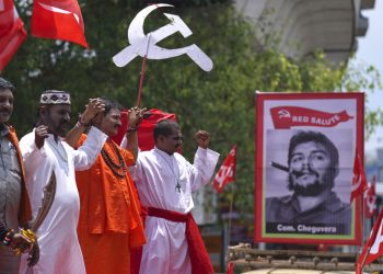 Členovia Centra indických odborov (CITU) oblečení ako moslimskí, hinduistickí a kresťanskí kňazi stoja vedľa obrazu kubánskeho revolučného vodcu Che Guevaru 1. mája 2023 (Foto: SITA/AP Photo/Mahesh Kumar A.)
