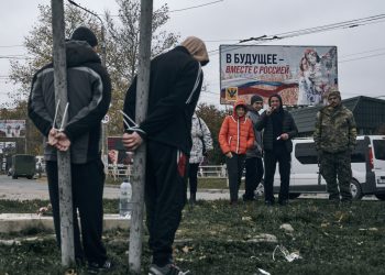 Ilustračný obrázok: Ukrajinský vojak a miestni obyvatelia sa pozerajú na dvoch údajných kolaborantov priviazaných za ruky k stĺpom v ukrajinskom Chersone v nedeľu 13. novembra 2022 (Foto: SITA/AP Photo/LIBKOS)