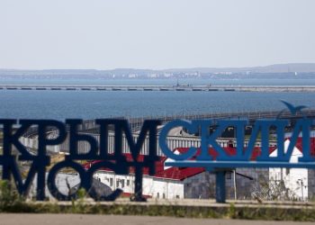 Poškodené časti automobilového spojenia, vpravo uprostred, Krymského mosta spájajúceho ruskú pevninu a Krymský polostrov cez Kerčský prieliv, v popredí nápis "Krymský most" z ruského mesta Taman v pondelok 17. júla 2023. Útok pred svitaním poškodil časť mosta spájajúceho Rusko s Moskvou anektovaným Krymom, ktorý je kľúčovou zásobovacou trasou (Foto: SITA/AP Photo)