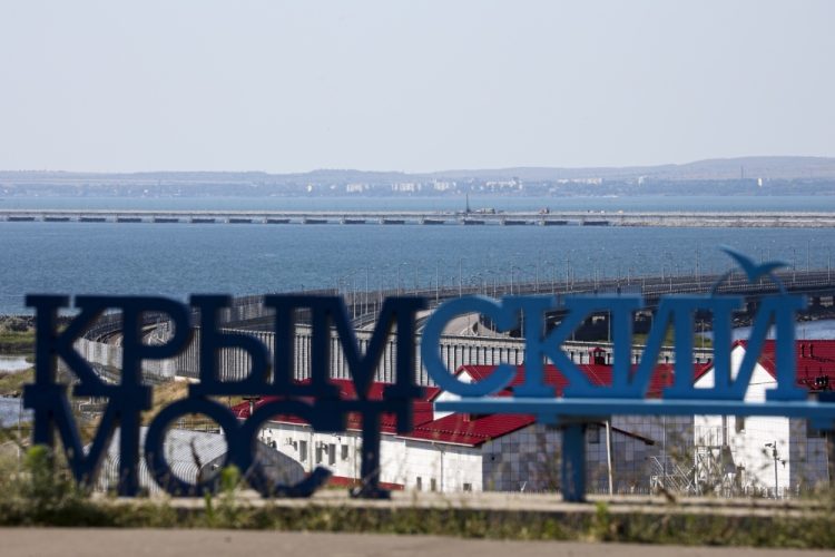 Poškodené časti automobilového spojenia, vpravo uprostred, Krymského mosta spájajúceho ruskú pevninu a Krymský polostrov cez Kerčský prieliv, v popredí nápis "Krymský most" z ruského mesta Taman v pondelok 17. júla 2023. Útok pred svitaním poškodil časť mosta spájajúceho Rusko s Moskvou anektovaným Krymom, ktorý je kľúčovou zásobovacou trasou (Foto: SITA/AP Photo)